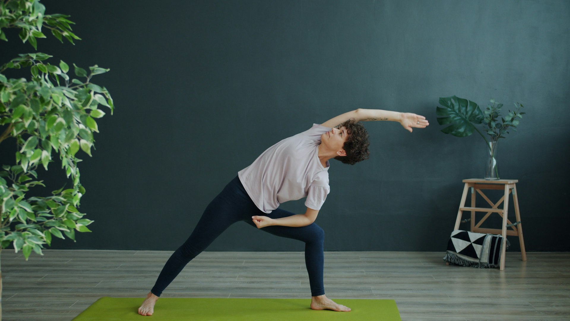 Woman on a green mat resting her lower forearm on her bent front thigh while her top arm reaches overhead