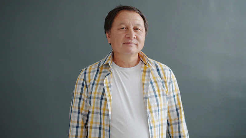 man smiling warmly in plaid shirt with gray backdrop
