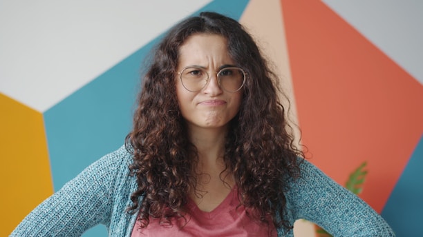 Woman with curly hair and glasses looks annoyed.