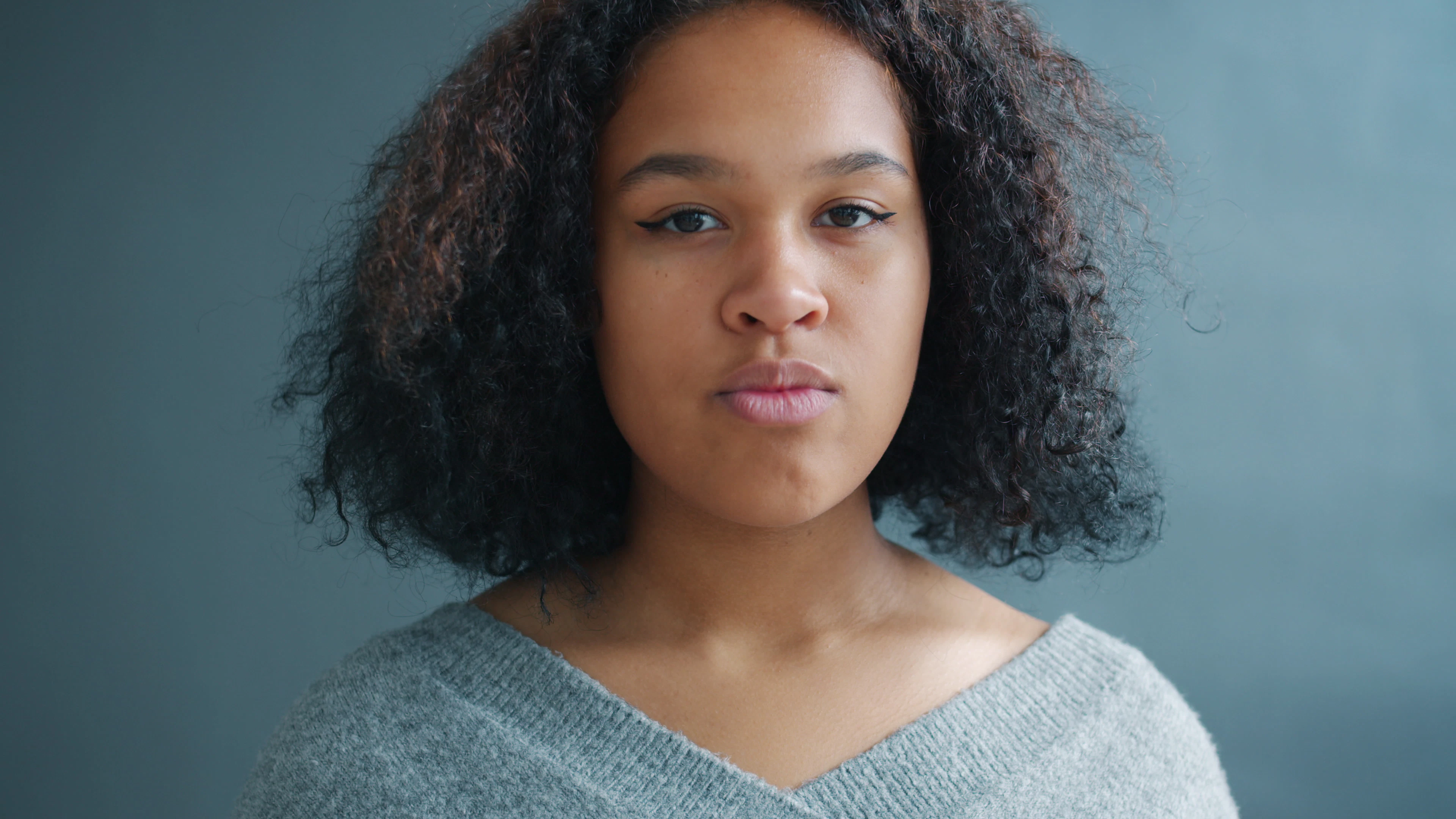Young woman with curly hair on a grey background, neutral expression