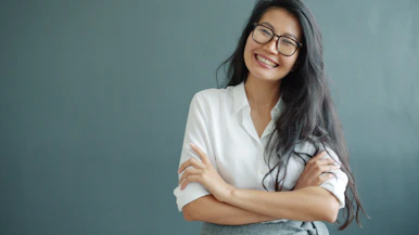 A smiling woman with glasses and arms crossed.