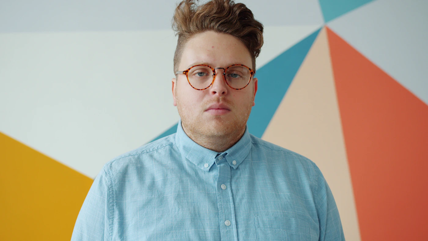 A person in glasses standing against a colourful wall