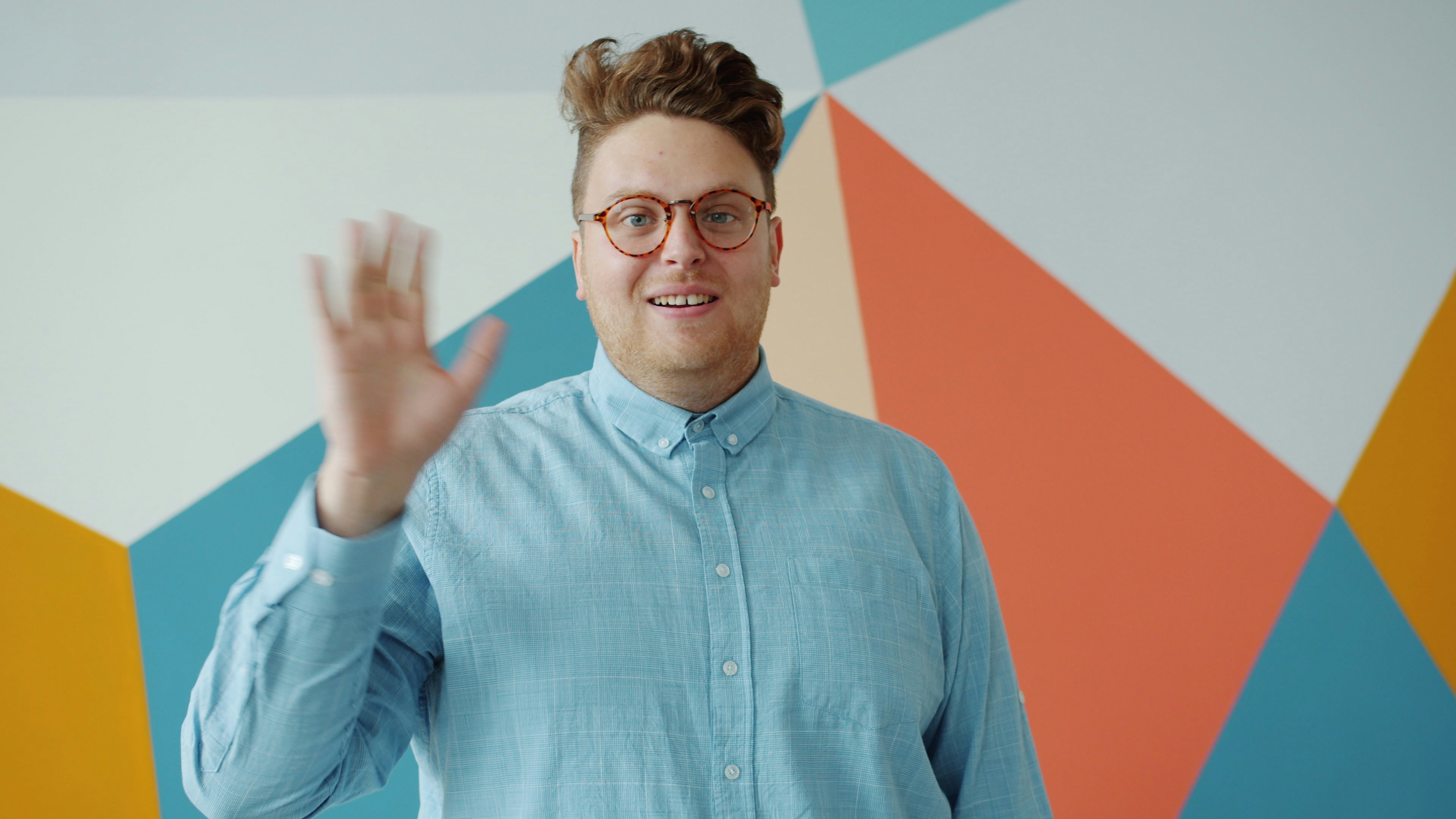Man in glasses waving hello in front of colorful wall