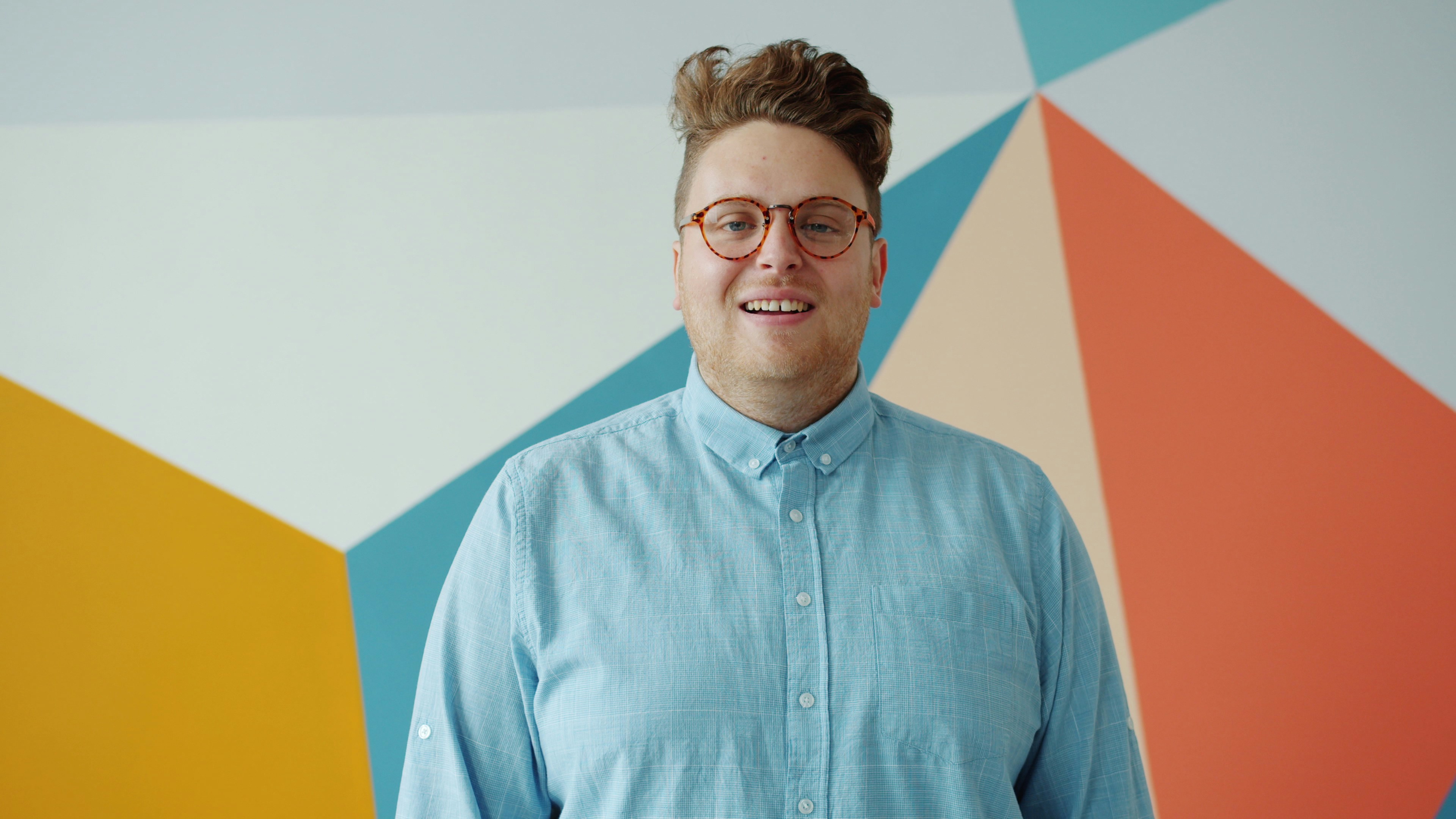 Man in blue shirt smiles against colorful geometric wall