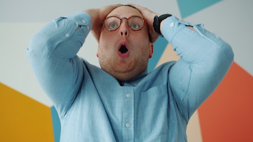 Man with glasses grabs head in shock