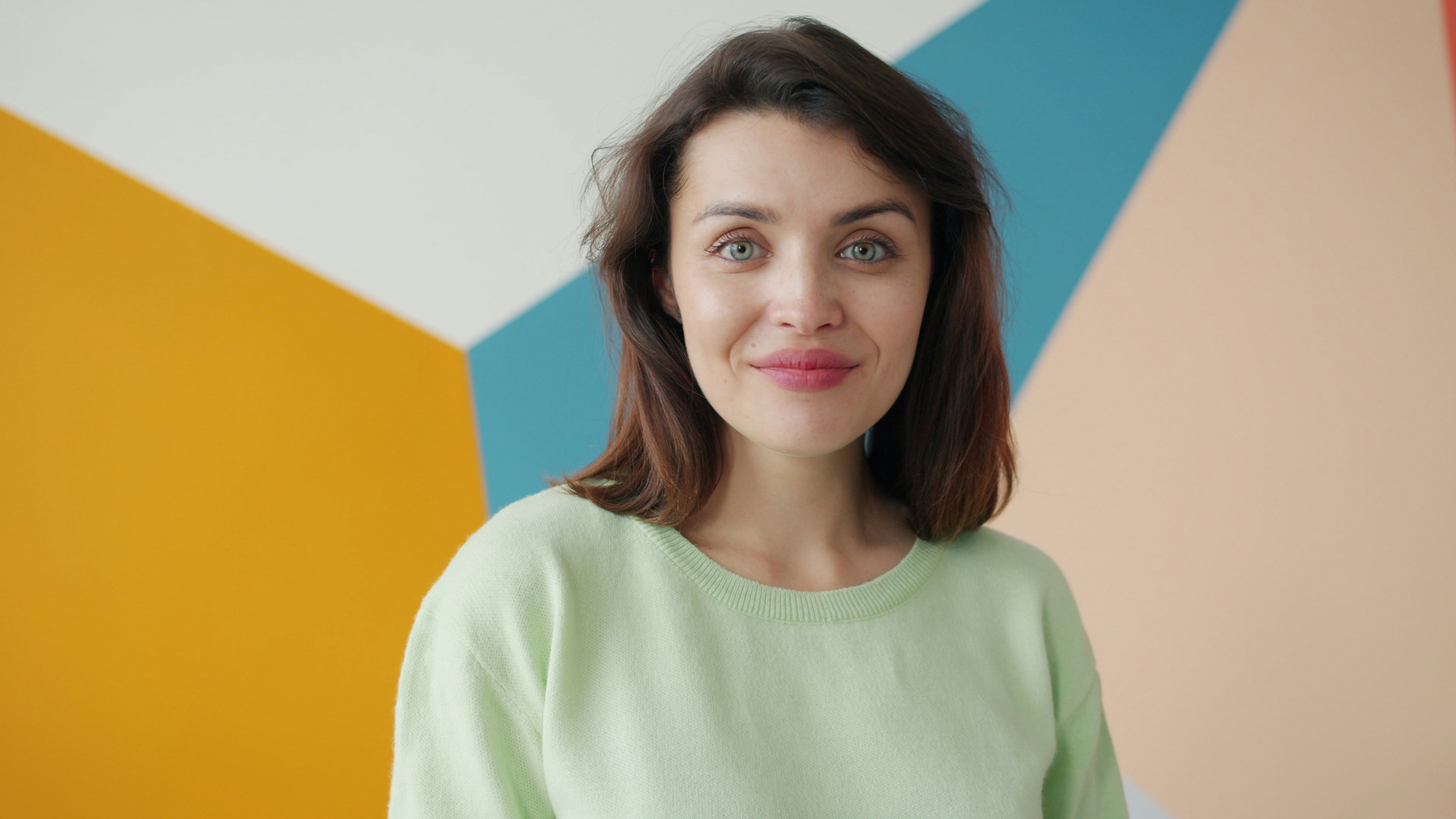Woman with brown hair smiles against colorful wall