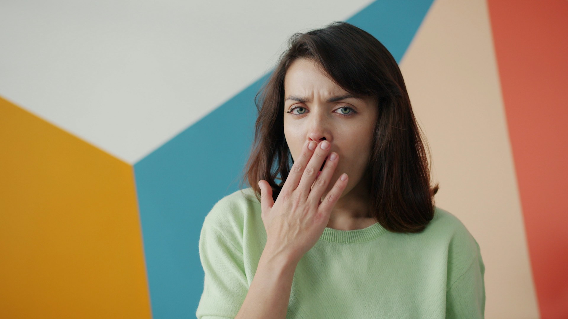 Woman covering mouth with hand, looking surprised.