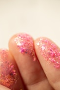 Pink glitter on fingers with a soft background
