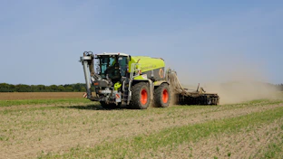 Tractor working in a field, kicking up dust.