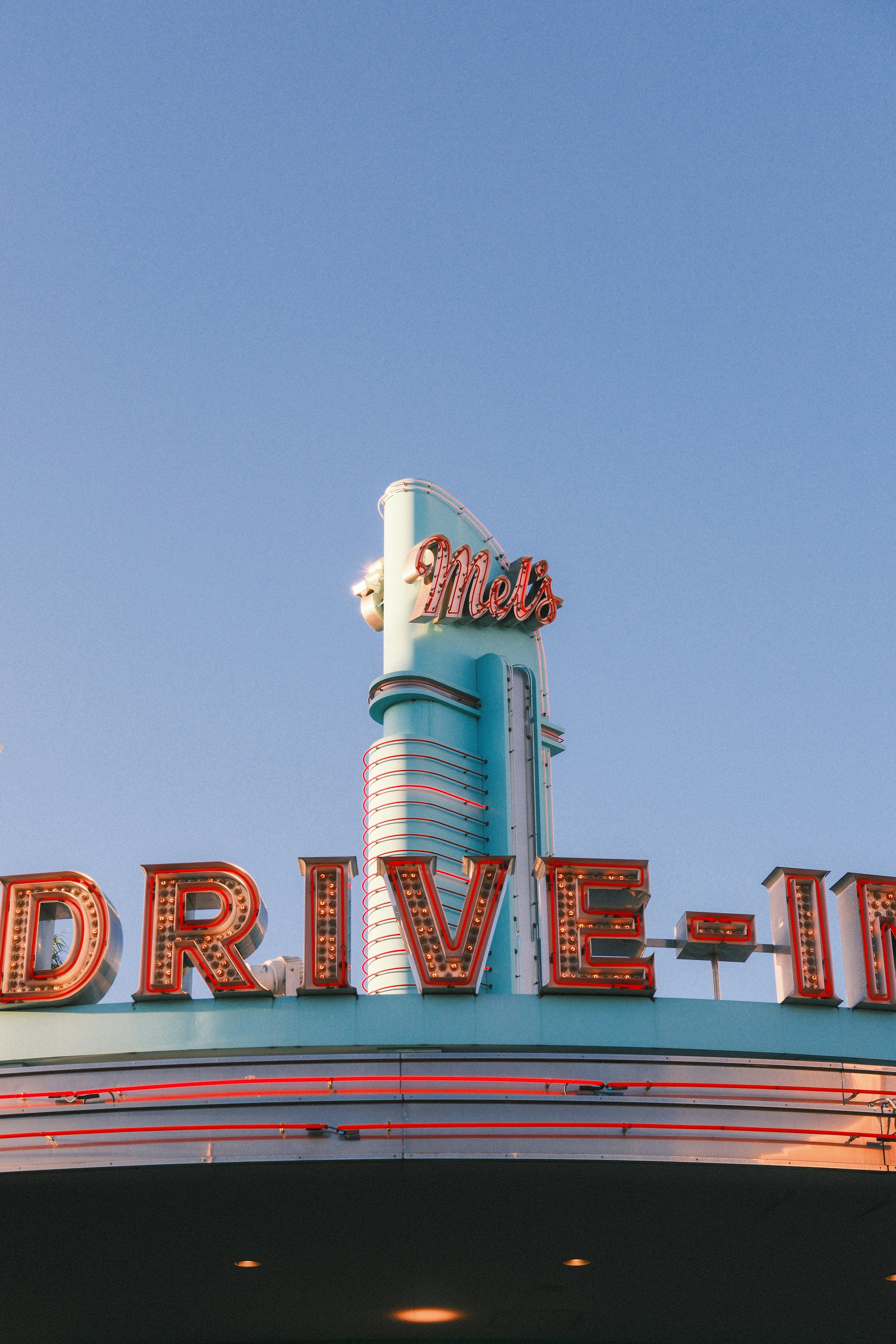 Retro drive-in sign with neon lights against blue sky