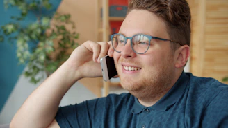 A man wearing glasses talks on his phone.