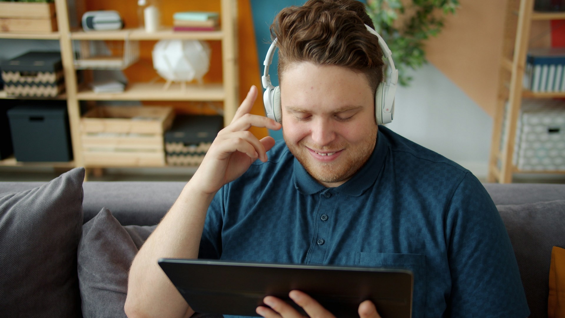 Man wearing headphones watches a tablet on couch.