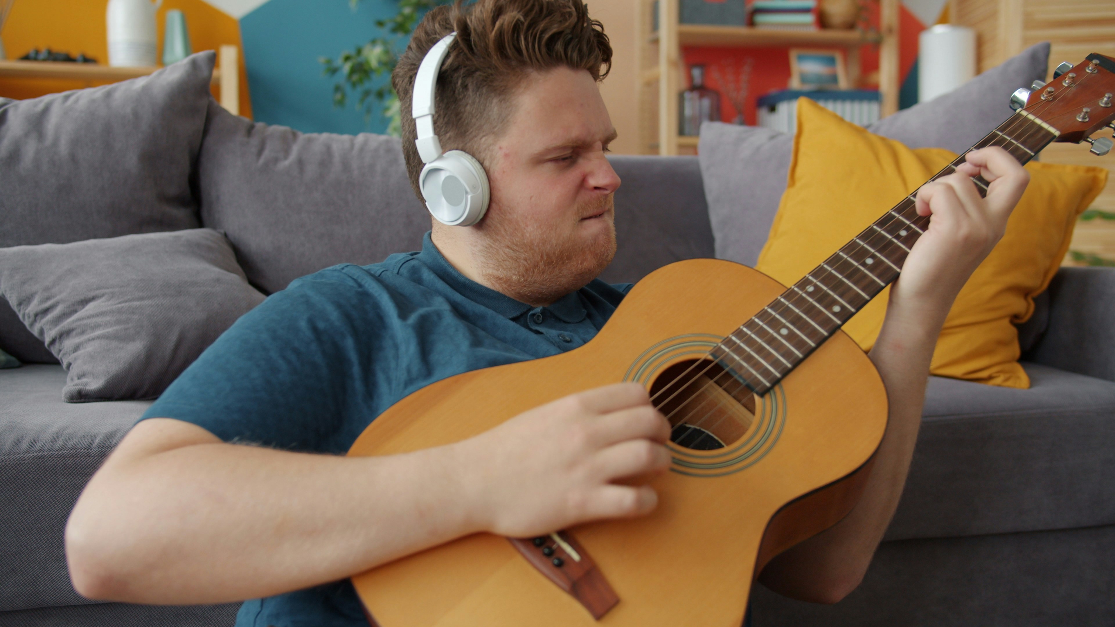 Man with headphones plays acoustic guitar at home