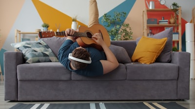 Young man playing guitar upside down on sofa.