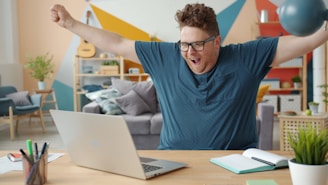 Man celebrating success while working on laptop at home.