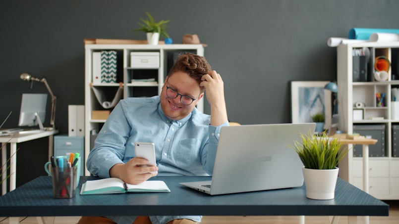 Man laughing while looking at his phone at desk.