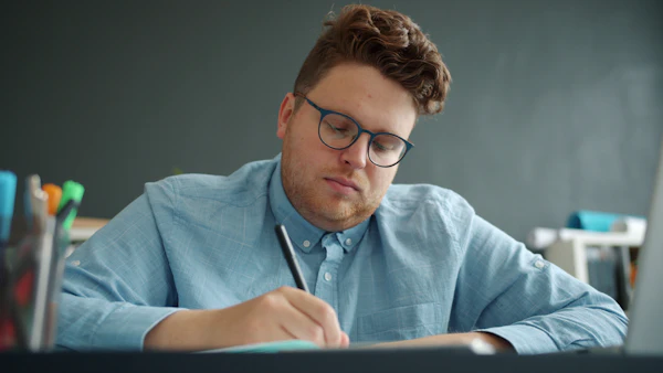 Un homme portant des lunettes écrit dans un cahier