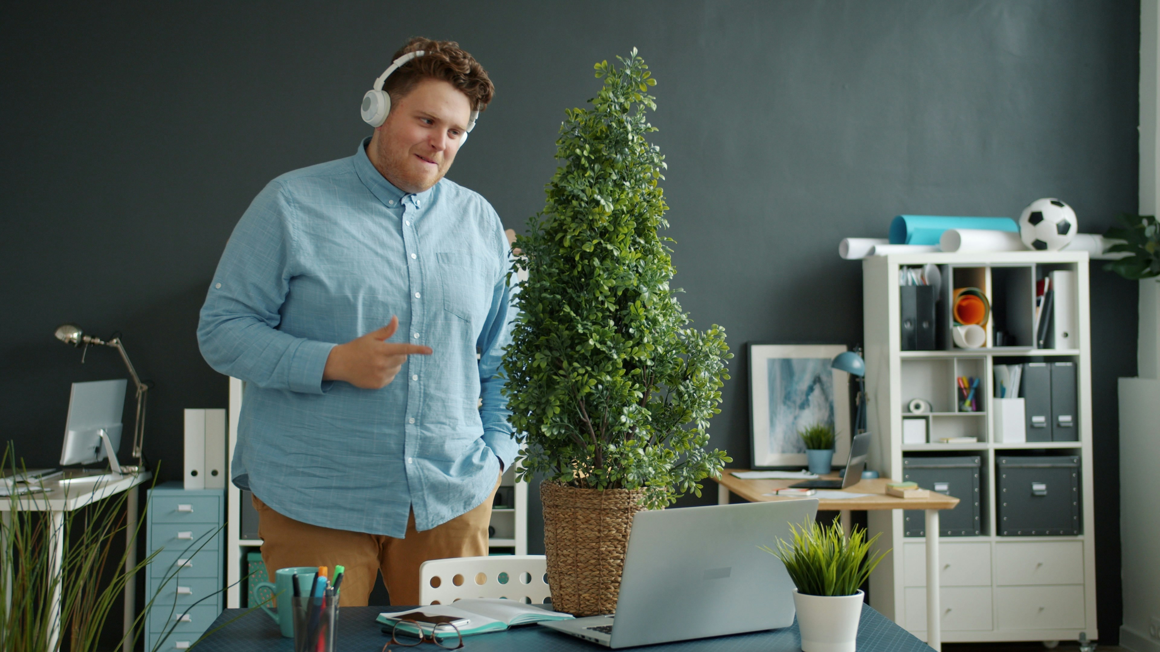Man in headphones standing by office desk with plant