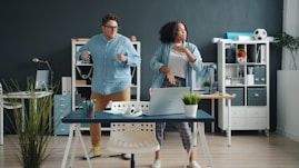 Two colleagues dancing energetically in a modern office.