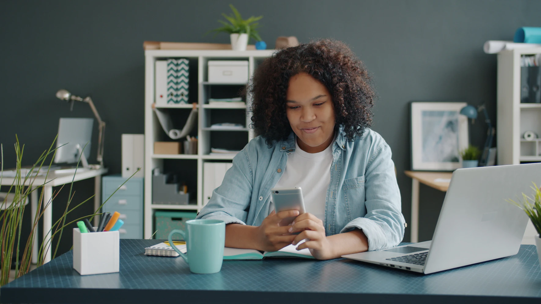 Person using a smartphone at a desk beside a laptop