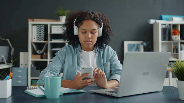 Young girl with headphones uses phone at desk