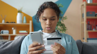Young woman holding credit card and smartphone indoors