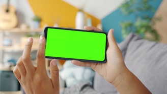 Person holding a smartphone with a green screen.