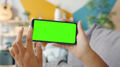Person holding a smartphone with a green screen.
