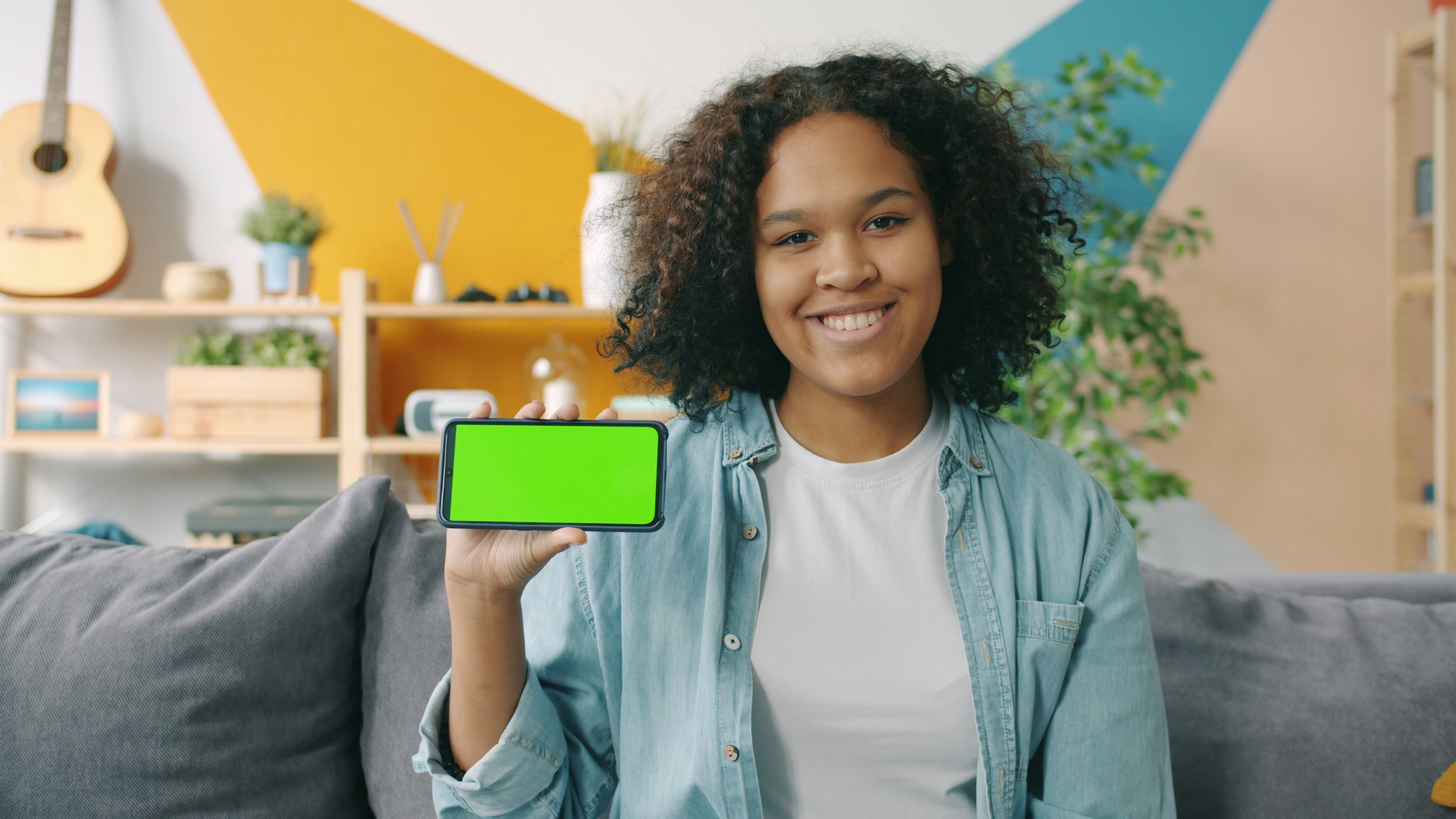 Portrait of happy Afro-American lady holding copy space green screen smartphone