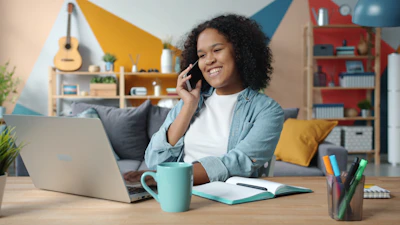 Woman talking on phone while working on laptop at desk.