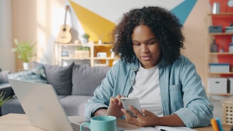 Young woman using phone at desk with laptop.