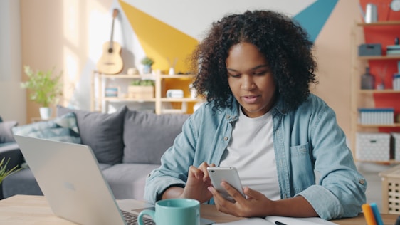 Young woman using phone at desk with laptop.