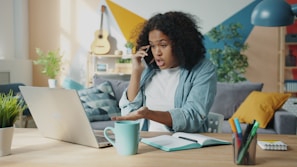 Young woman talking on phone at laptop desk.
