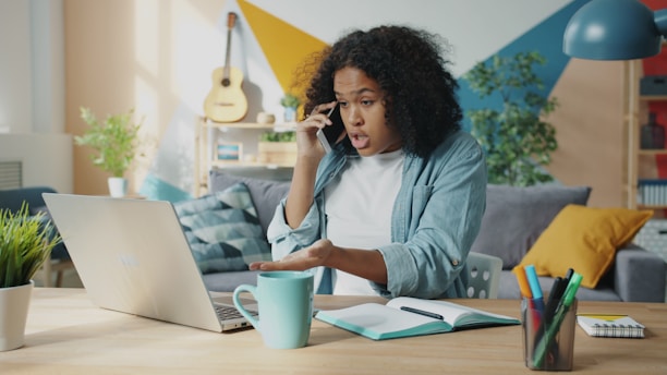 Young woman talking on phone at laptop desk.