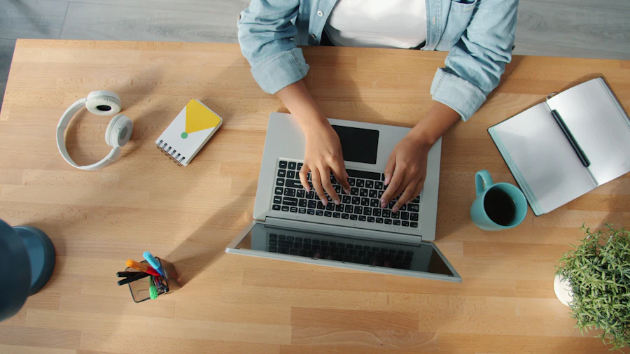 A person typing content on a laptop at a wooden desk