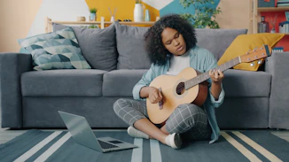 Young woman learning to play guitar from laptop