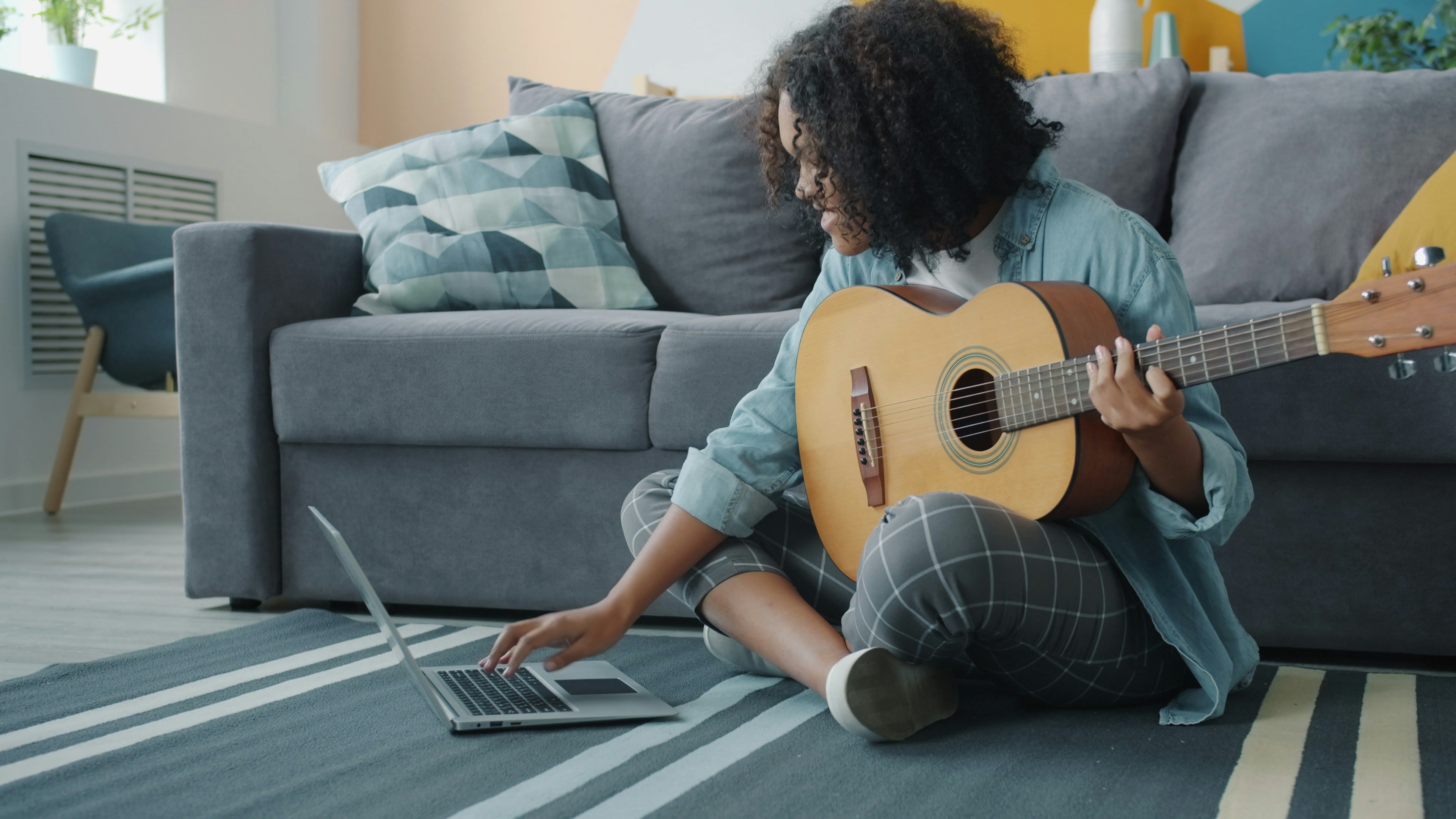 Woman playing guitar and using laptop on floor