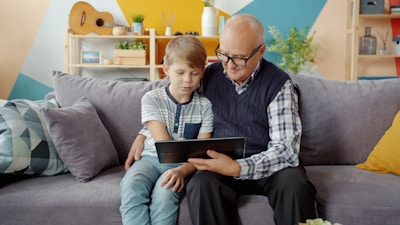 Grandfather and grandson looking at tablet together on sofa.