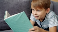 A young boy reading a book on a couch.