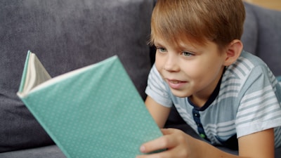 A young boy reading a book on a couch.