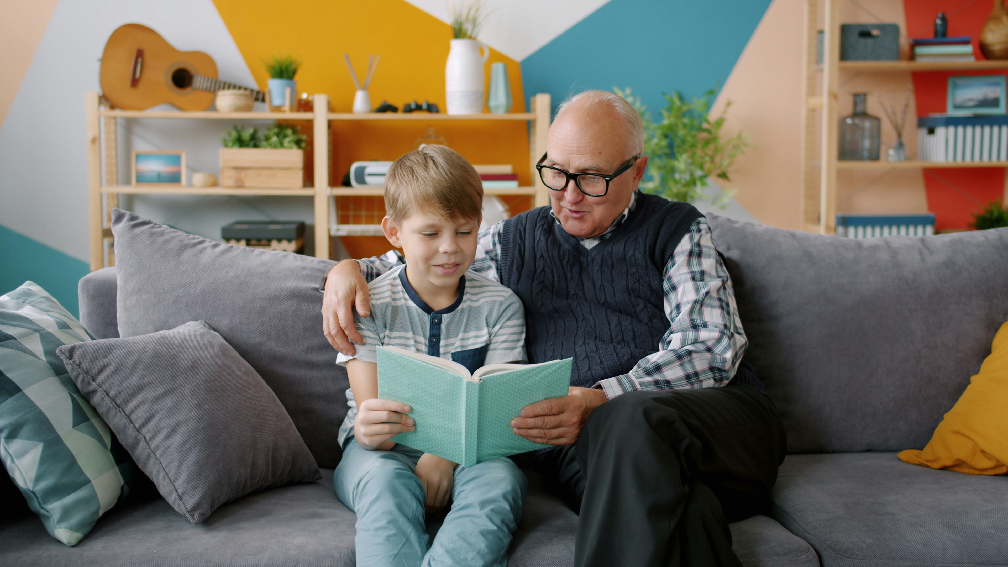 Grandfather and grandson reading a book together on couch