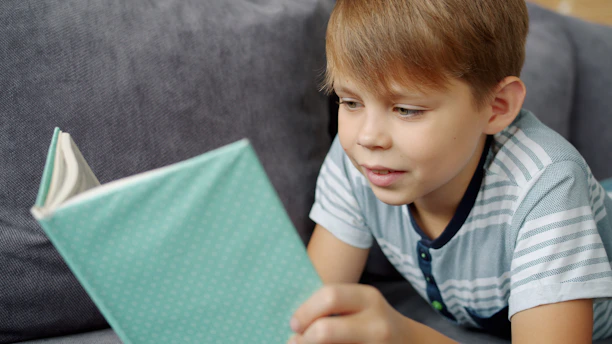 A young boy reads a book on a couch