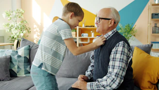 Boy adjusting grandfather's collar while sitting on couch.