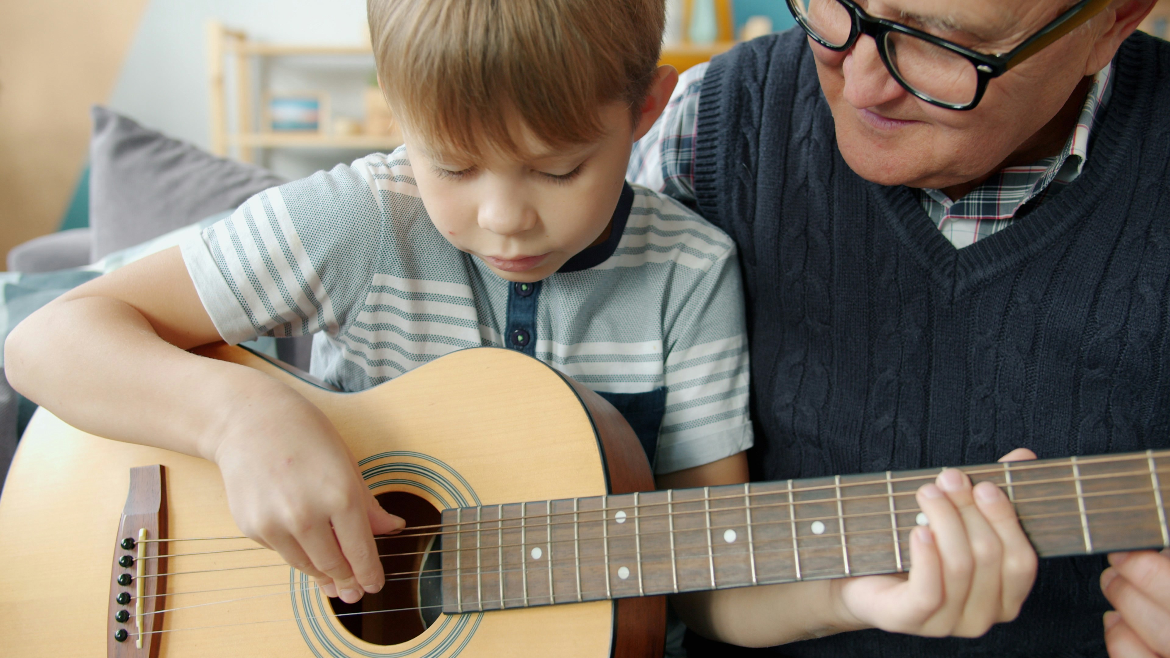 Grandfather teaching grandson guitar at home
