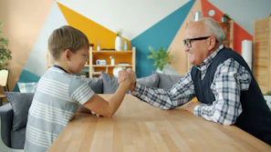 Grandfather and grandson arm wrestling at table.