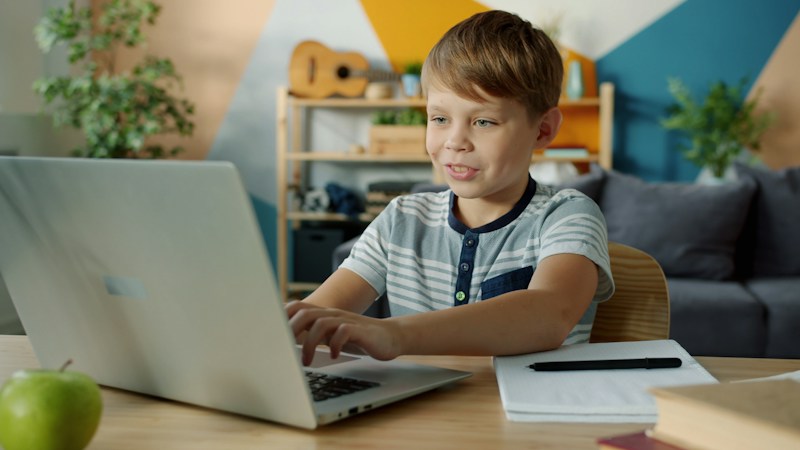 A high school student working on a laptop at a kitchen table during a virtual school day