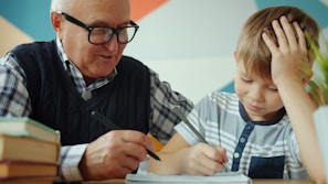 Grandfather helps grandson with homework at table