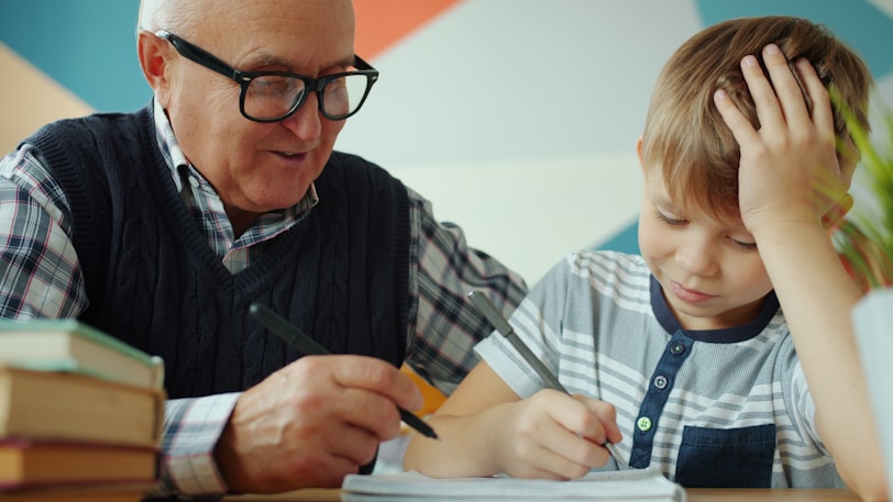 Grandfather helps grandson with homework at table