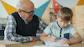 Grandfather helping grandson with homework at table.