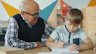 Grandfather helping grandson with homework at table.